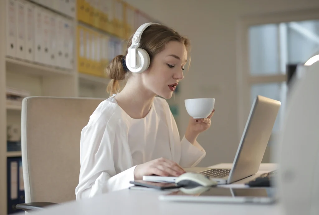 A young woman working on her laptop while sipping hot chocolate and wearing headphones, creating a cozy and focused writing environment.